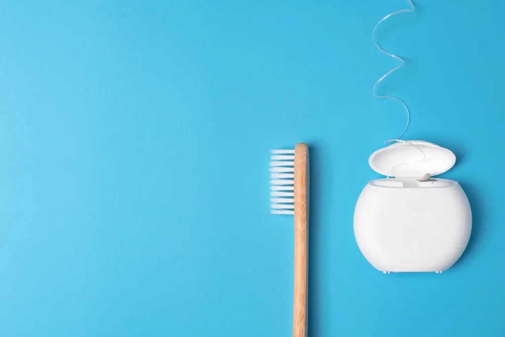 A bamboo toothbrush and dental floss on a blue background, essential tools for preventing the stages of gum disease and maintaining oral health. Big Sky Family Dental promotes these daily oral hygiene practices.