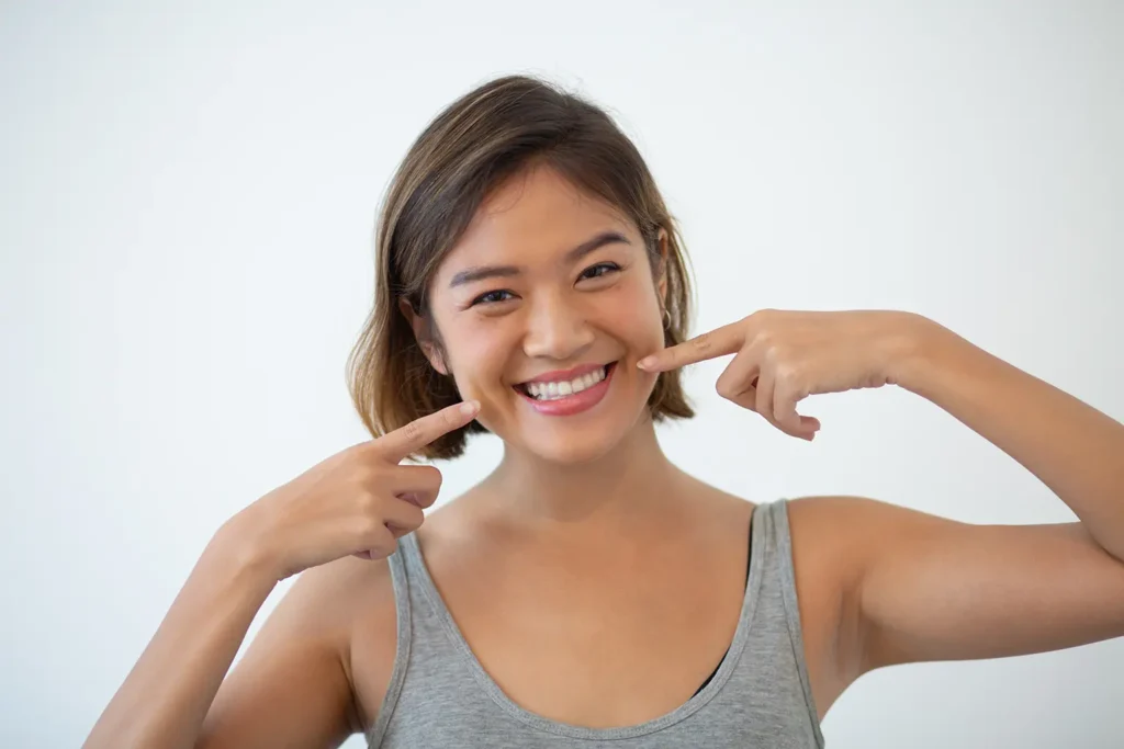 Smiling woman pointing at her teeth, showcasing the importance of oral health. Big Sky Family Dental highlights the heart connection and overall health benefits of good dental care.