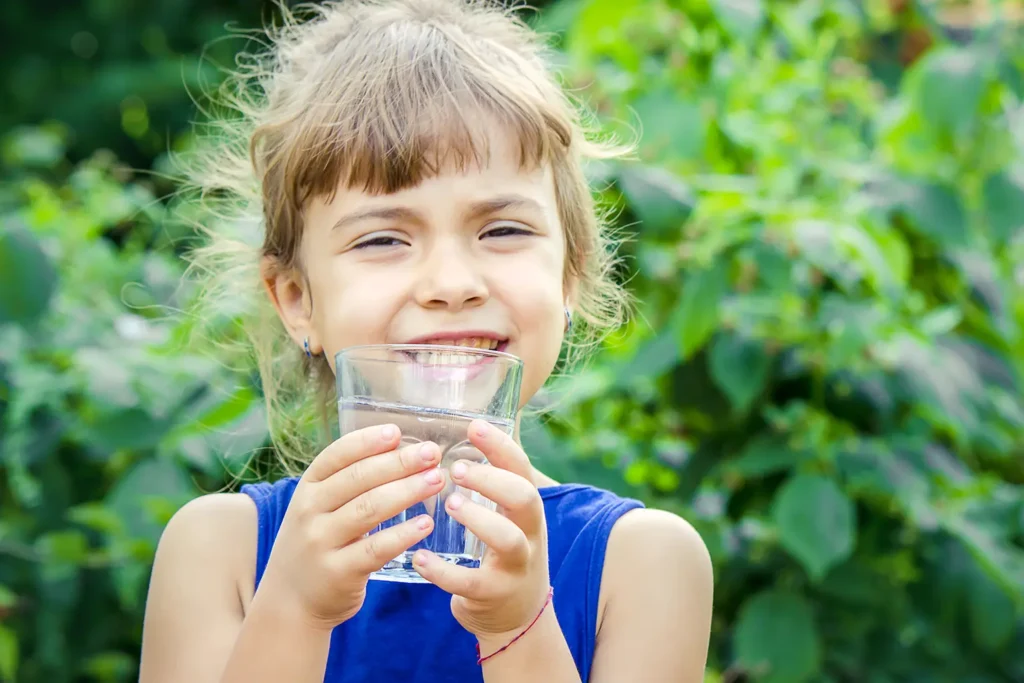 Young girl smiling and drinking water, highlighting the importance of hydration as part of a healthy and balanced diet for maintaining oral health, supported by Big Sky Family Dental.