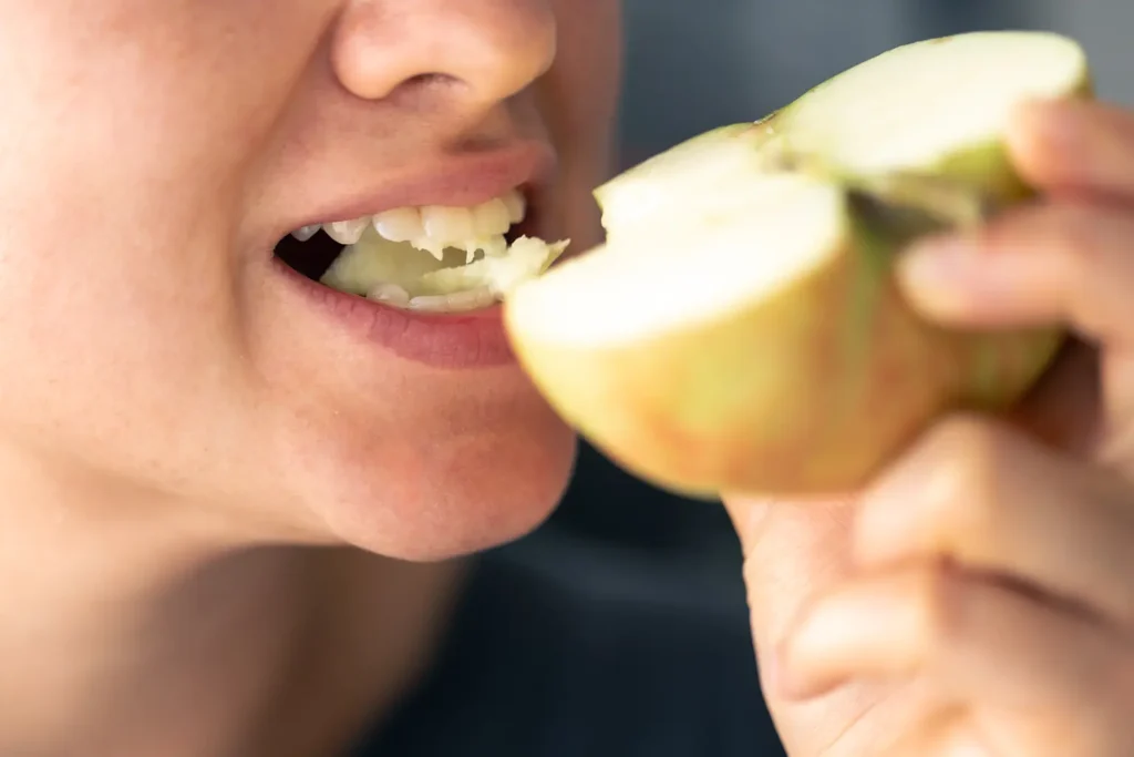 Close-up of a woman experiencing a dental issue while biting into an apple, highlighting the need for emergency dental services at Big Sky Family Dental in Billings, MT