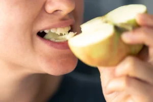 Close-up of a woman experiencing a dental issue while biting into an apple, highlighting the need for emergency dental services at Big Sky Family Dental in Billings, MT