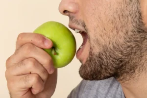 Close-up of a man biting a green apple, illustrating how to strengthen teeth through healthy eating habits, promoted by Big Sky Family Dental.